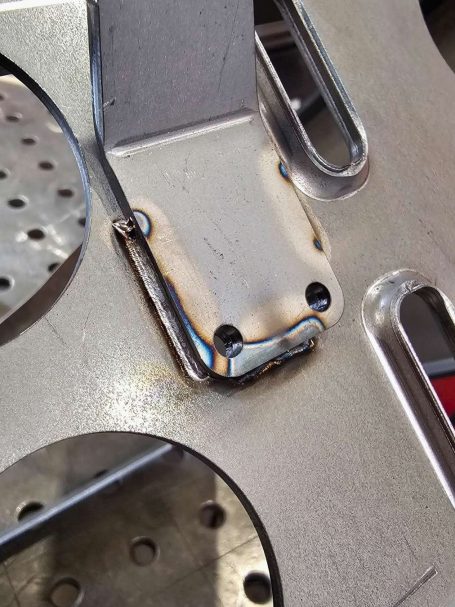 Lasergeschweißtes Bauteil Nahaufnahme von geschweißtem Metall mit runden Löchern und Schrauben.