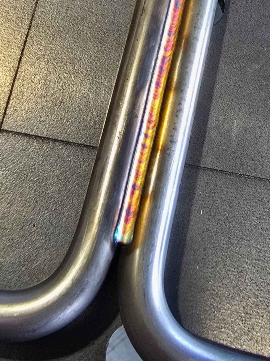 Lasergeschweißtes Rundmaterial Verbindung zweier metallischer Rohre auf einem schwarzen Bodenbelag.