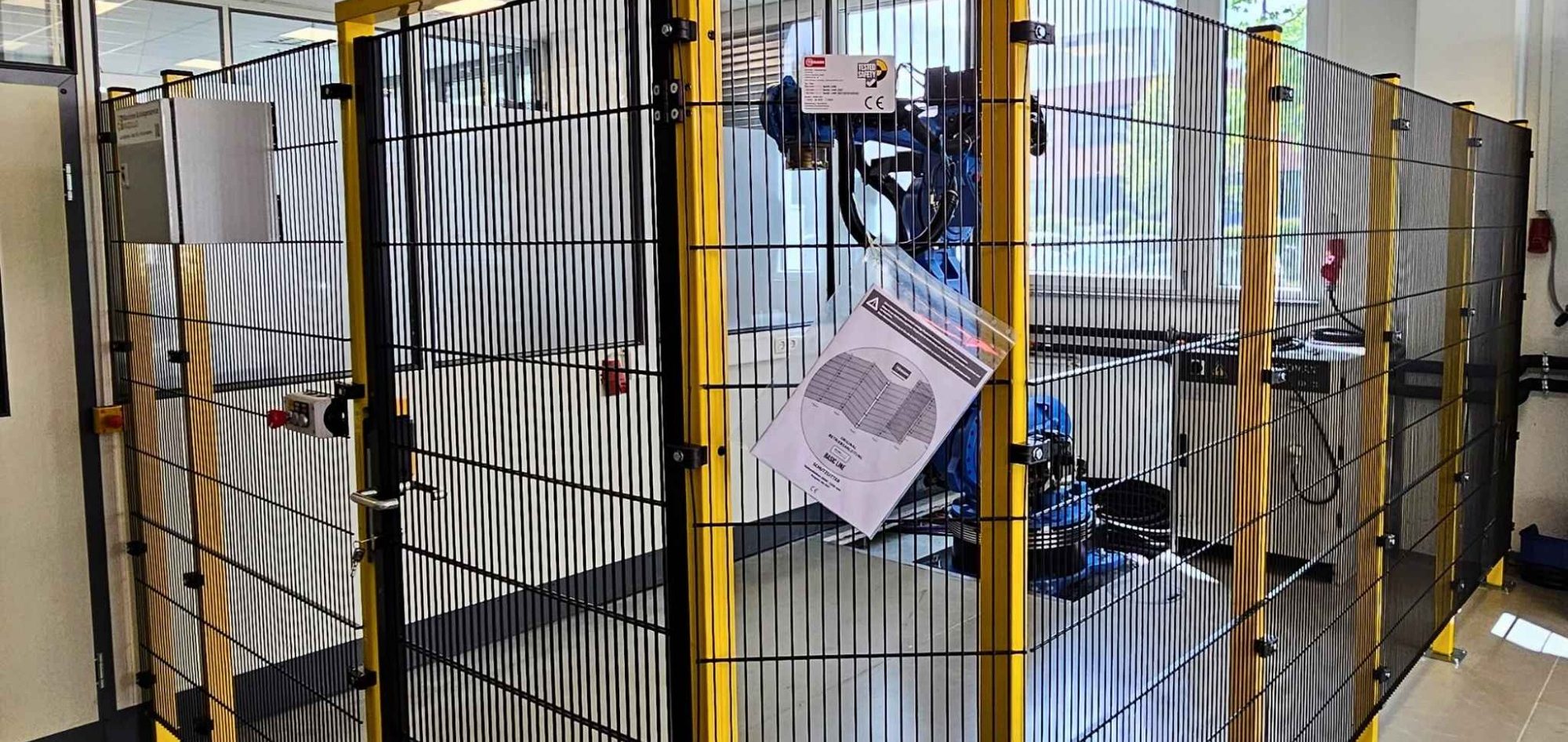 Roboterzellen und Roboteranlagen Roboterzelle mit Sicherheitszaun und Warnhinweisen im Hintergrund.