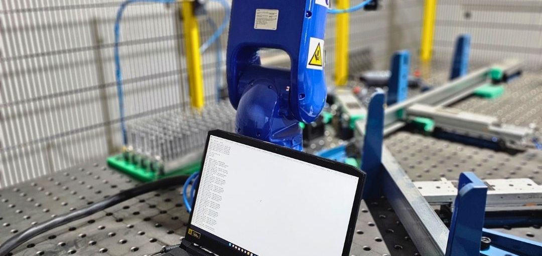 Roboterarm und Laptop auf einer Werkbank in einer Industrieumgebung.
