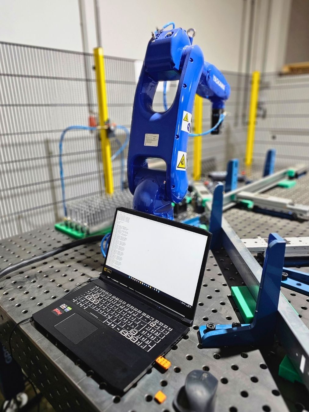 Blauer Industrieroboter Yaskaw neben einem Laptop auf einem Arbeitstisch.