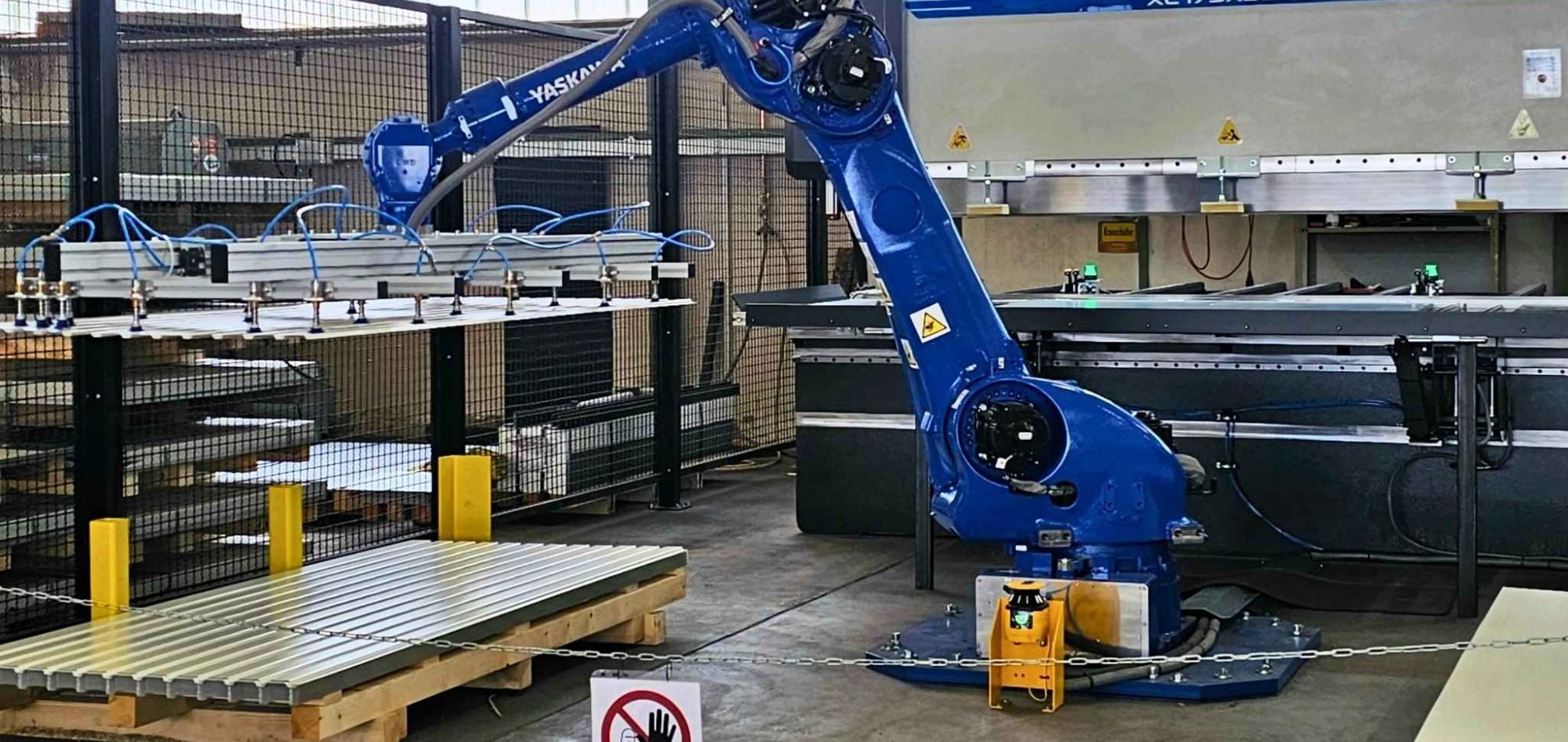Yaskawa GP180 in Roboterzelle Blauer Industrieroboter in einer Lagerhalle mit gestapelten Materialien.
