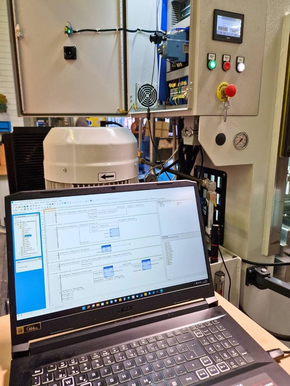 SPS und Roboterprogrammierung Laptop mit Steuerungssoftware vor einer industriellen Maschine mit Bedienelementen.