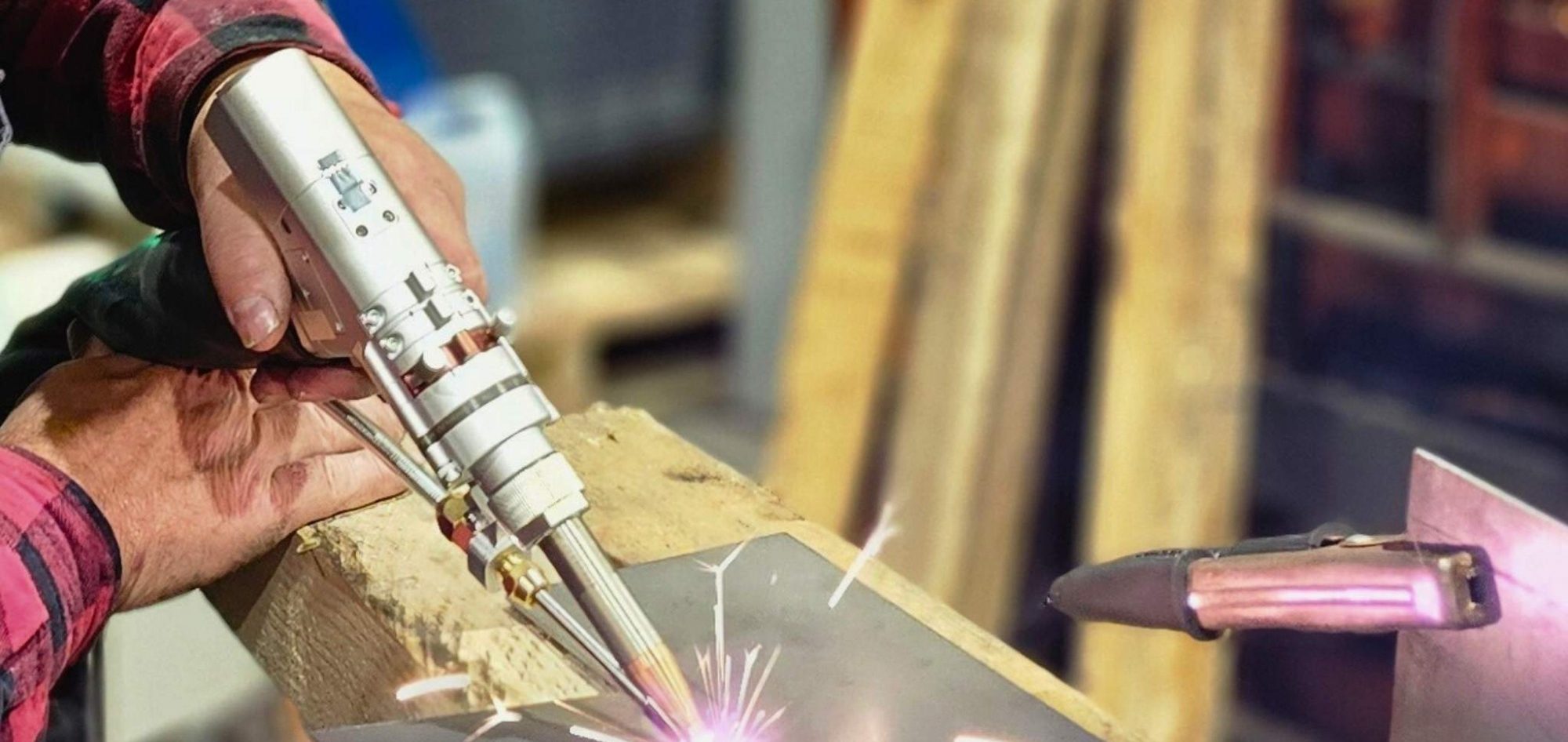 Hände halten ein Schweißgerät, das Funken erzeugt, während es auf einem Metallblech arbeitet.